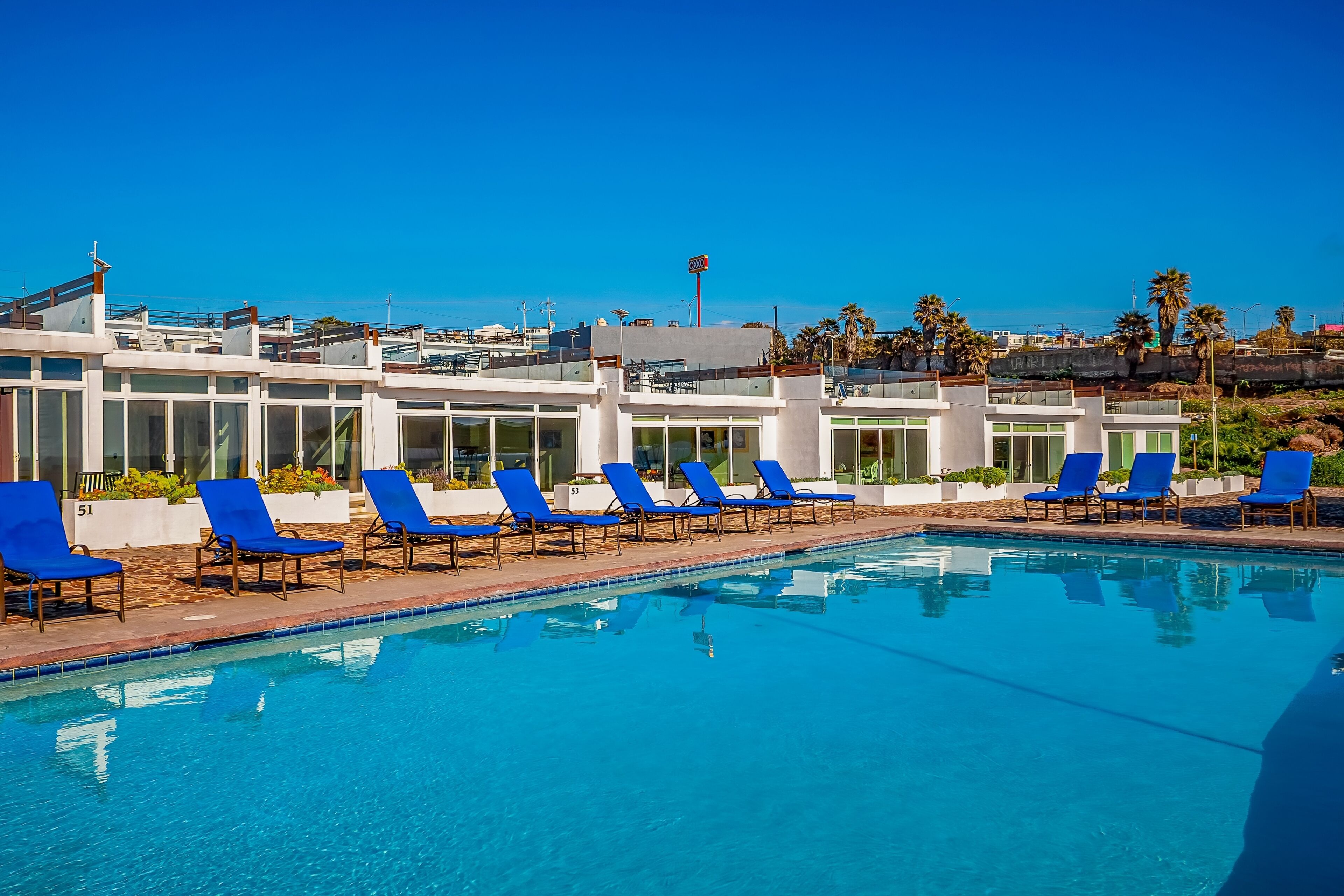 A swimming pool with blue lounge chairs and a modern building in the background.