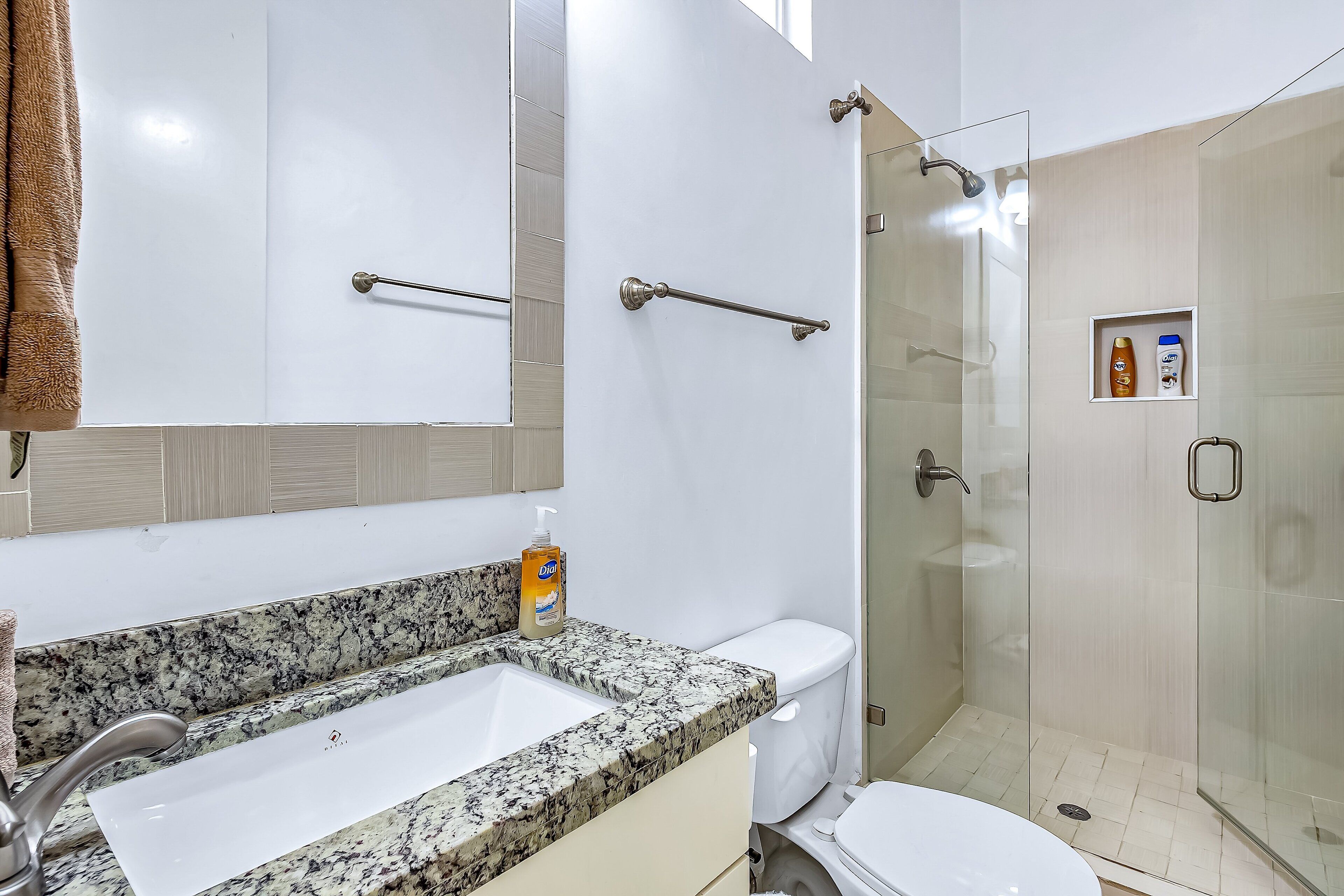 A bathroom with a granite countertop sink, a toilet, a glass shower enclosure, and a mirror.