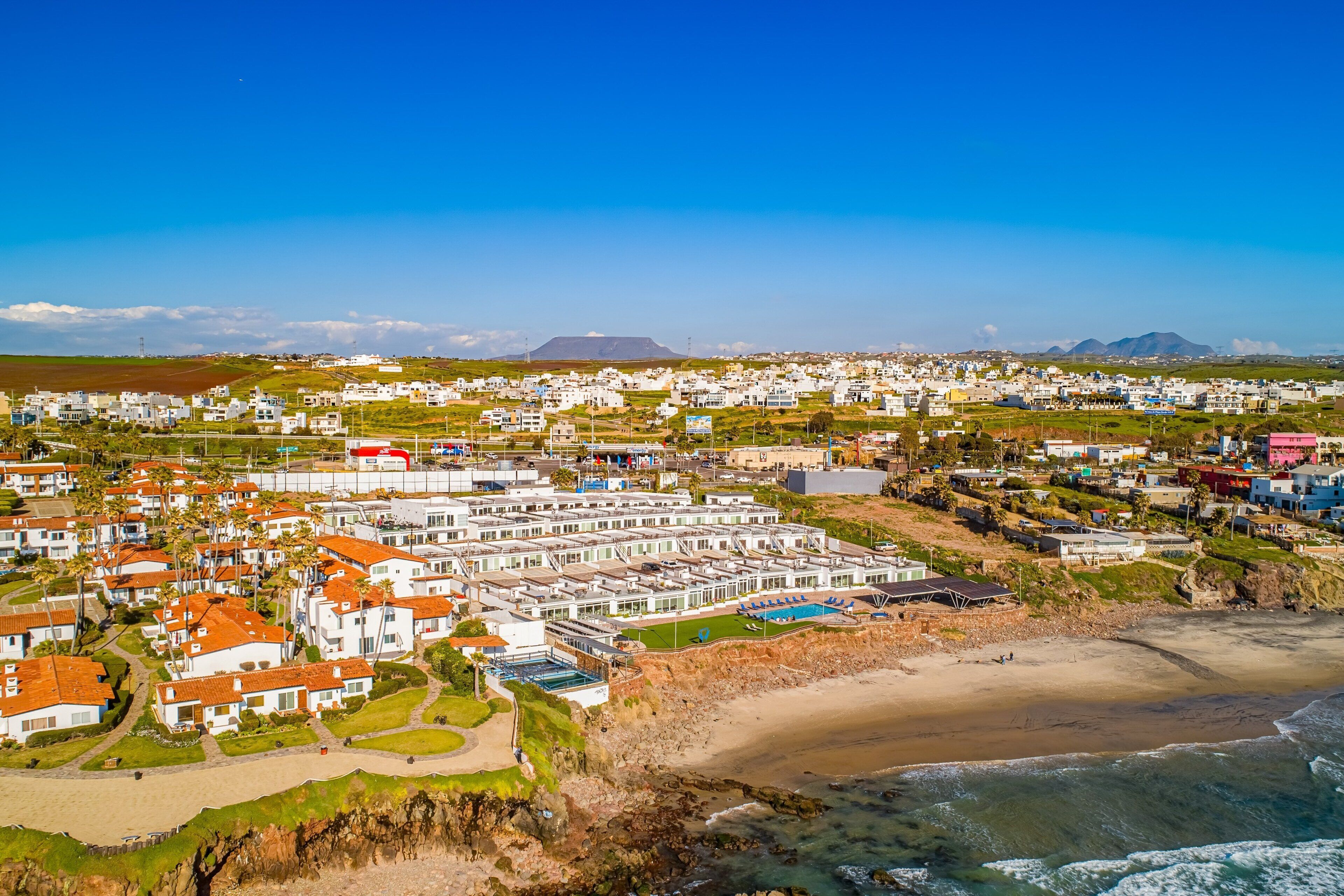 A coastal residential area with white buildings, a beach, and a clear blue sky.