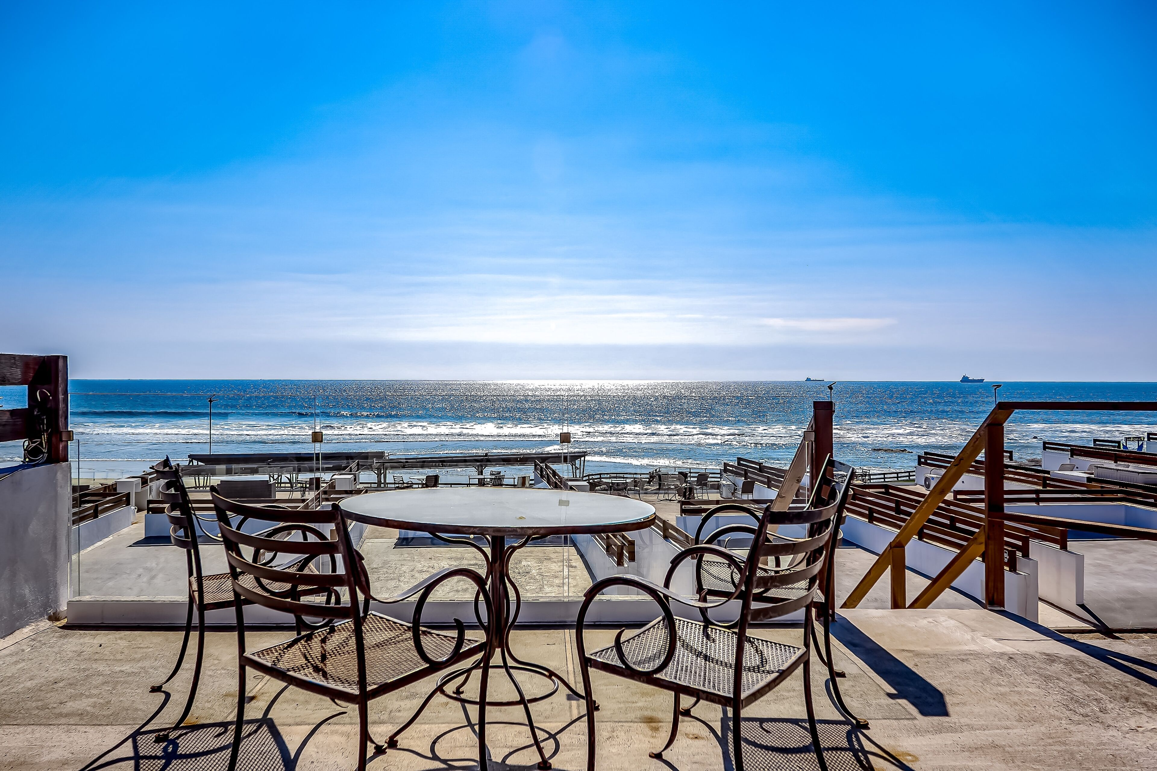 Une terrasse offrant une vue sur l’océan, avec des tables rondes et des chaises en métal.