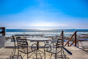 Eine Terrasse mit Blick auf den Ozean, ausgestattet mit runden Tischen und Metallstühlen.
