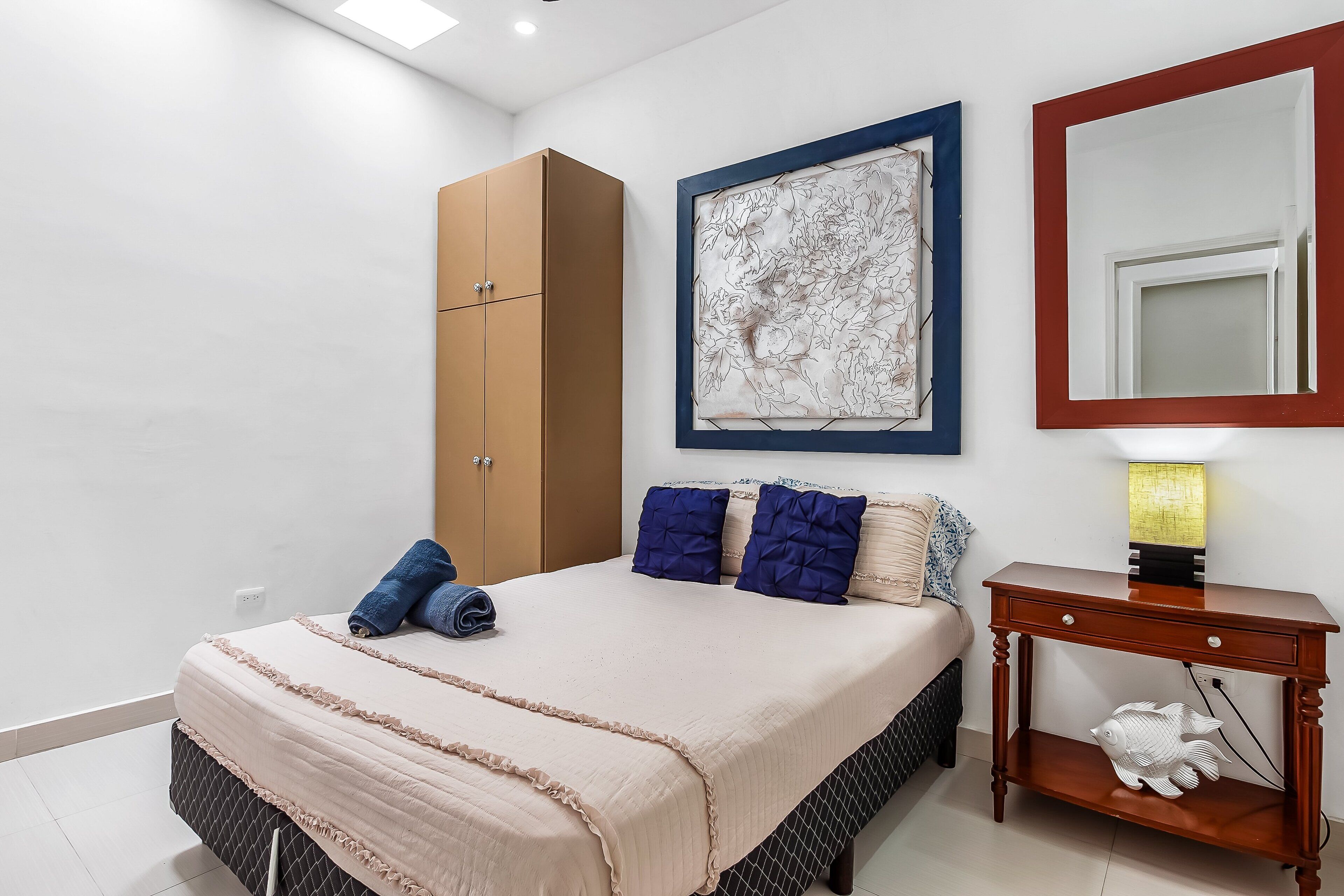 Een slaapkamer met een bed, een kledingkast, een kunstwerk in een lijst, een nachtkastje en een decoratie van een vis.