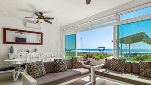 Ein modernes Wohnzimmer mit einer Couch, Esstisch, Stühlen und großen Fenstern mit Blick auf das Meer.