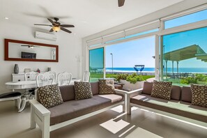 Ein modernes Wohnzimmer mit einer Couch, Esstisch, Stühlen und großen Fenstern mit Blick auf das Meer.