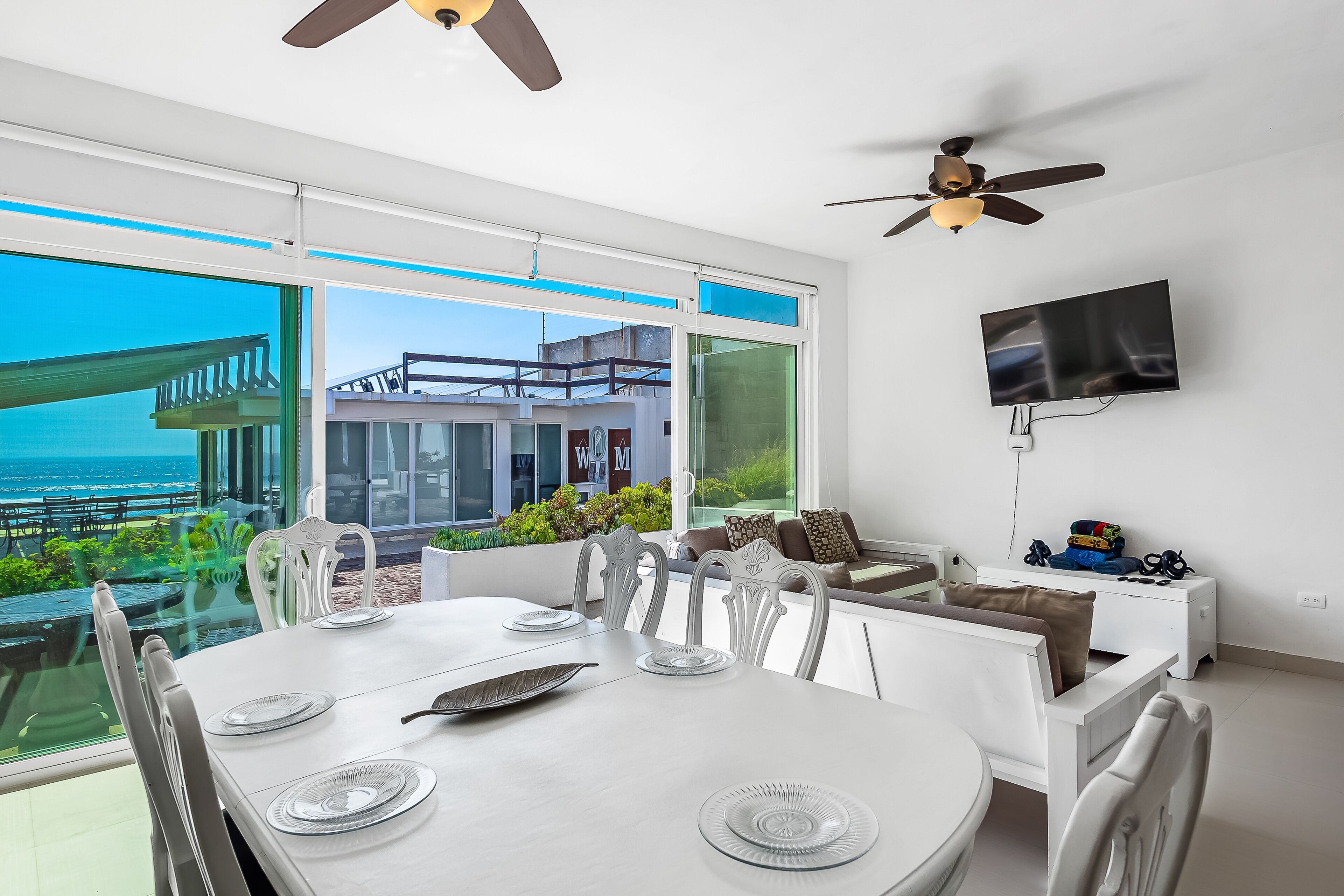 Un comedor moderno con una gran mesa, sillas blancas y vista al océano.