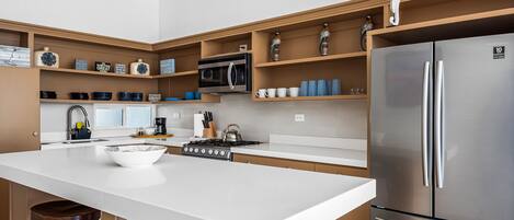 A modern kitchen with a central island, stainless steel appliances, and wooden shelves.