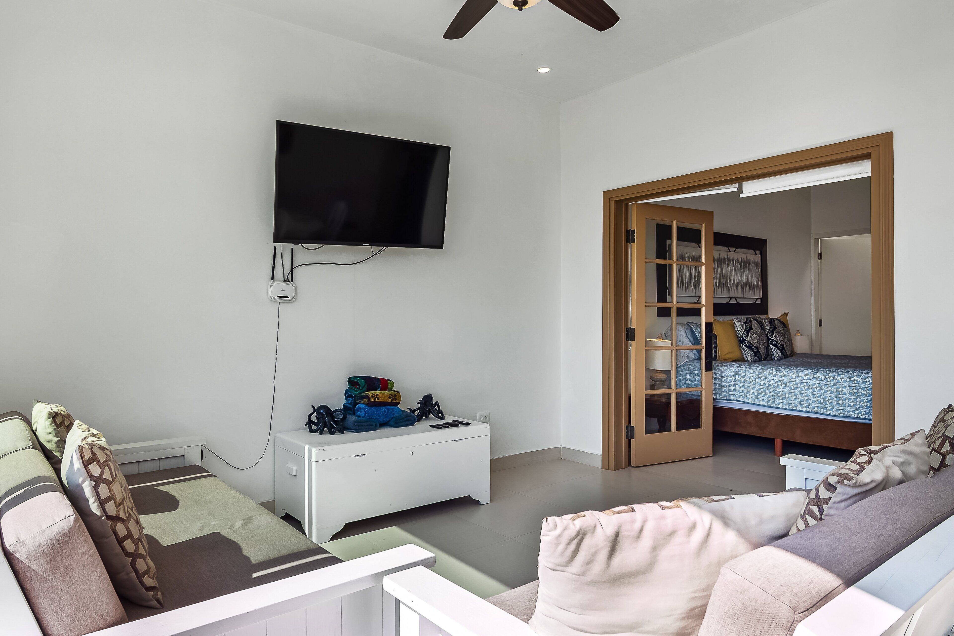 Een kamer met een bed, een televisie aan de muur, een witte ladekast en een bank.