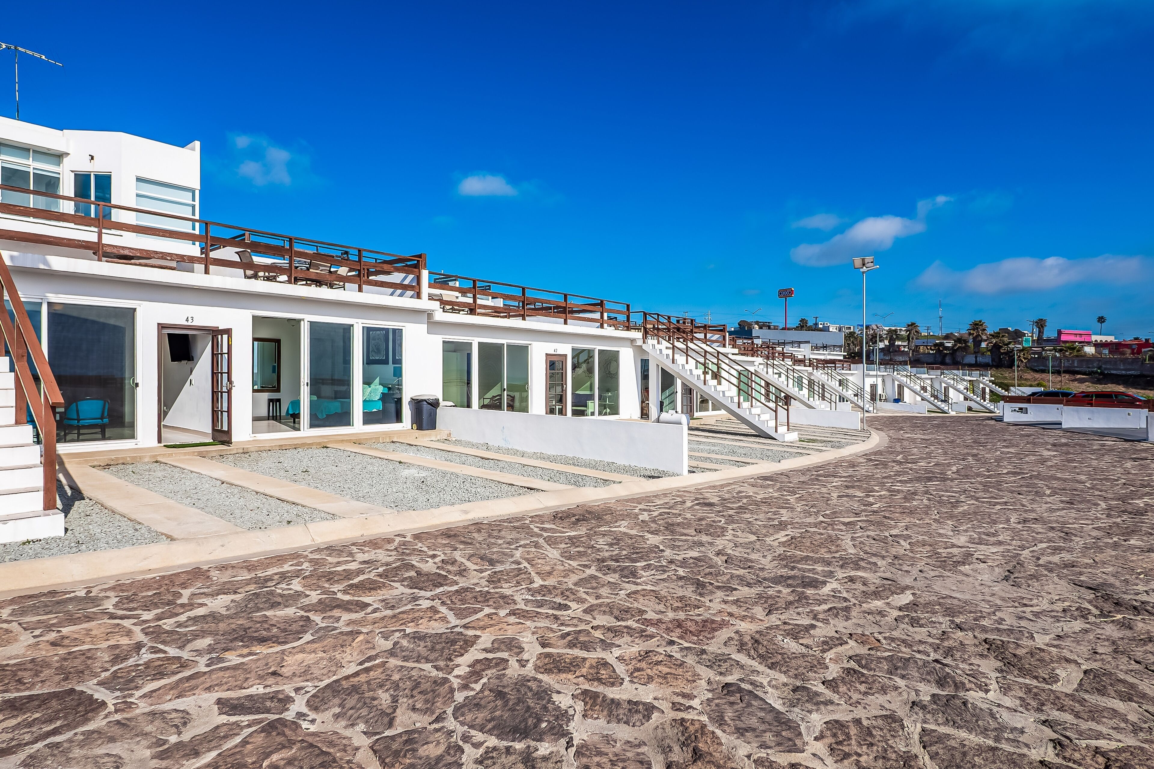 Un edificio moderno con un piano terra in pietra squadrata, una scala che conduce a un patio, e un cielo azzurro intenso.