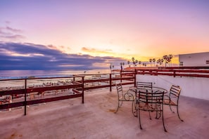 Una terrazza sul tetto con vista sull'oceano, un tavolo con sedie e una ringhiera.