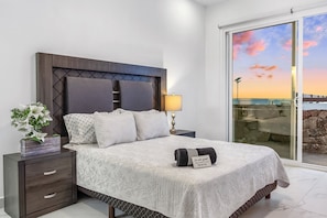 Una camera da letto con un letto, un comodino, una lampada e vista sul cielo attraverso una porta in vetro.