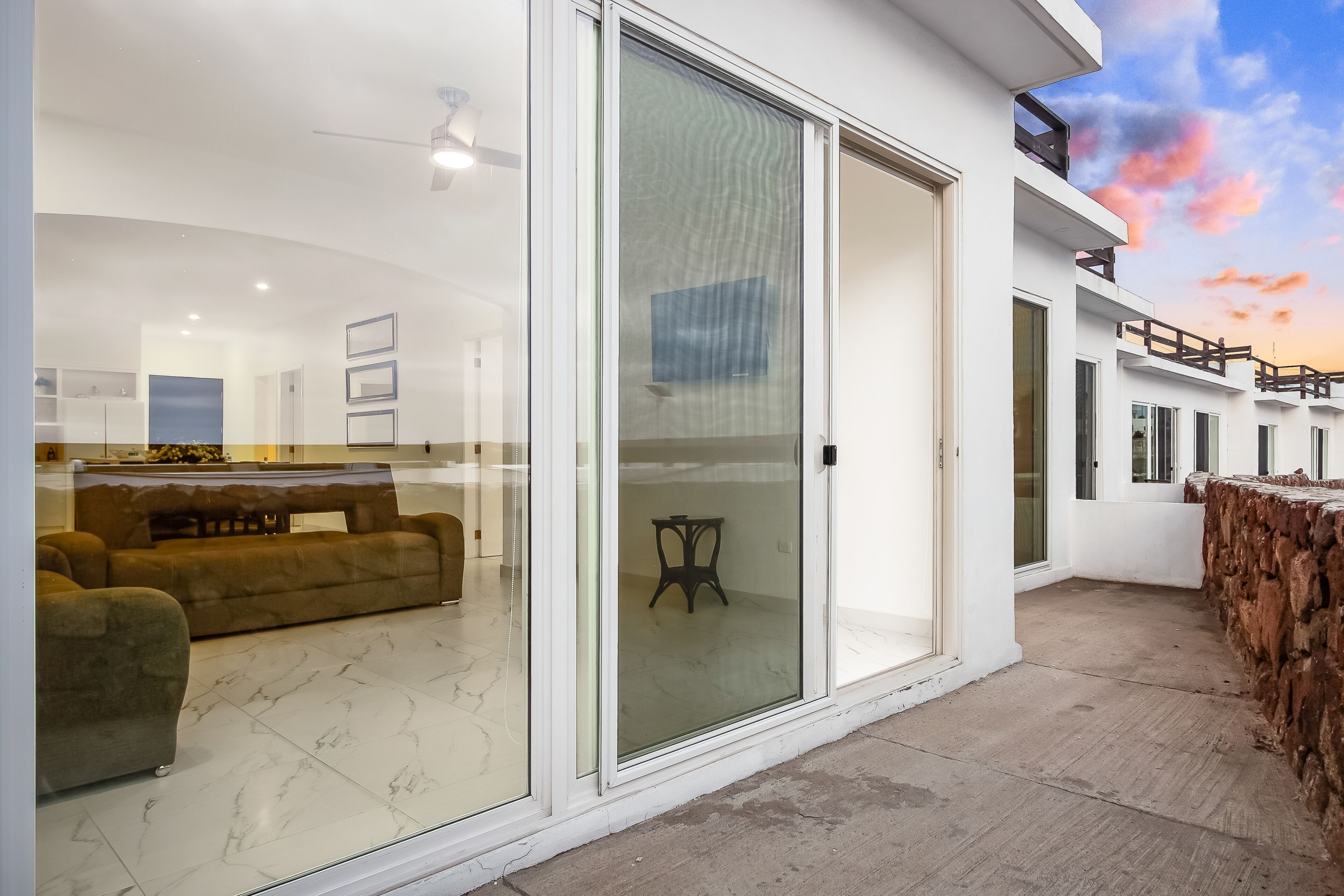 Un intérieur moderne avec un canapé et une table, une porte vitrée donnant sur un espace extérieur et un balcon doté d’une rambarde en bois.
