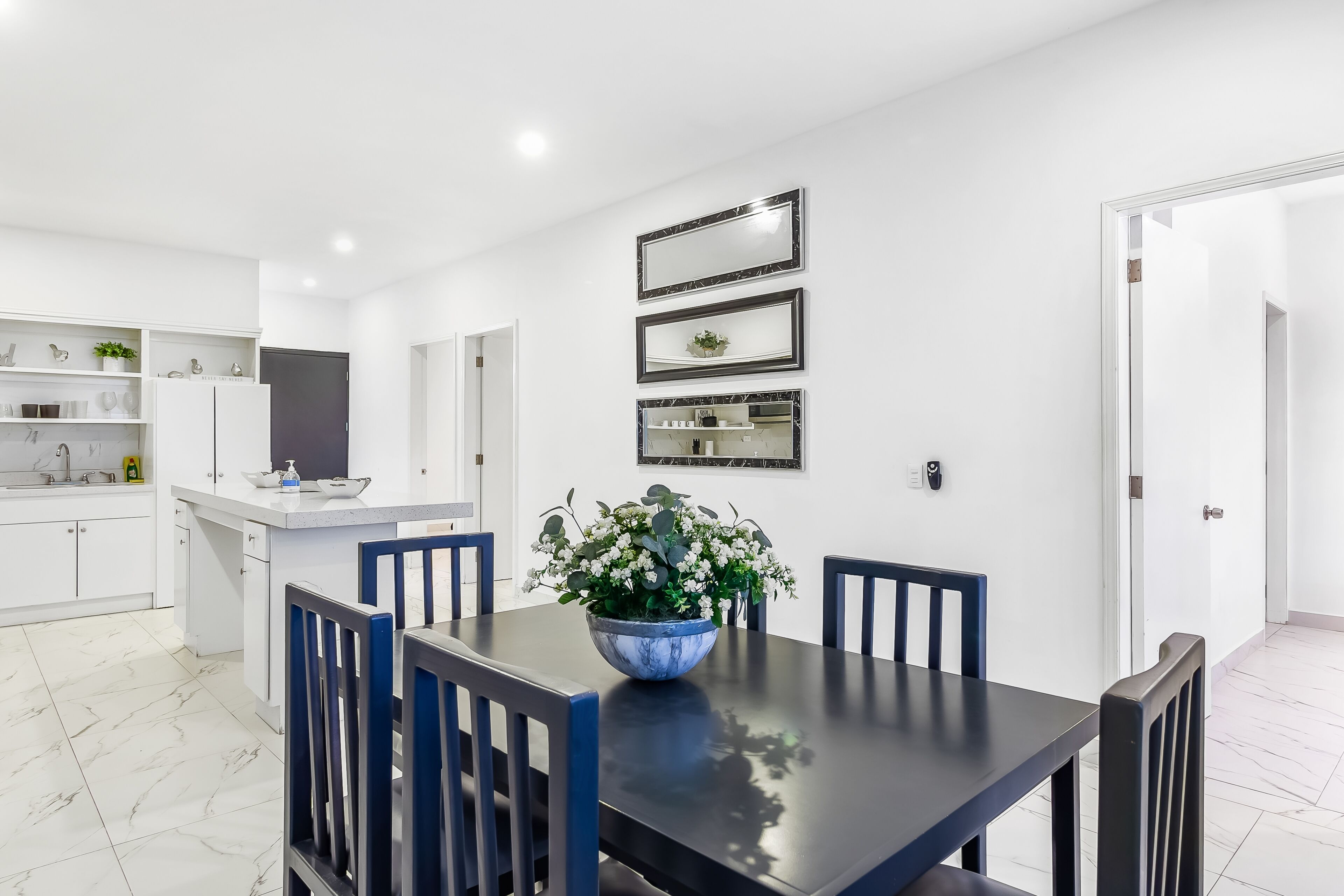 A modern kitchen with white cabinets, a marble-tiled floor, and a dining area with a dark table and blue chairs.