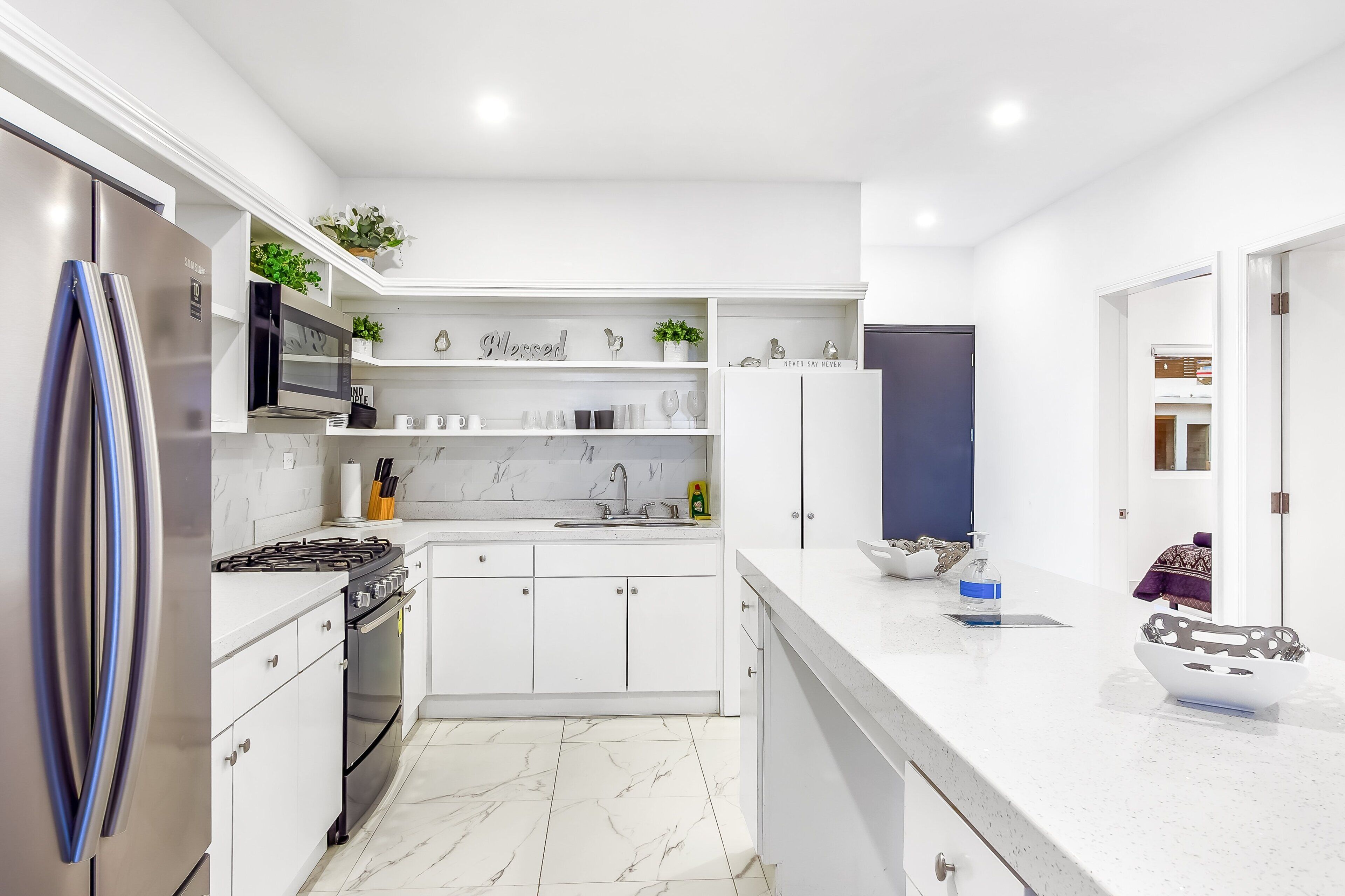 Una cocina moderna con armarios blancos, un refrigerador de acero inoxidable, una estufa a gas y piso de mármol.