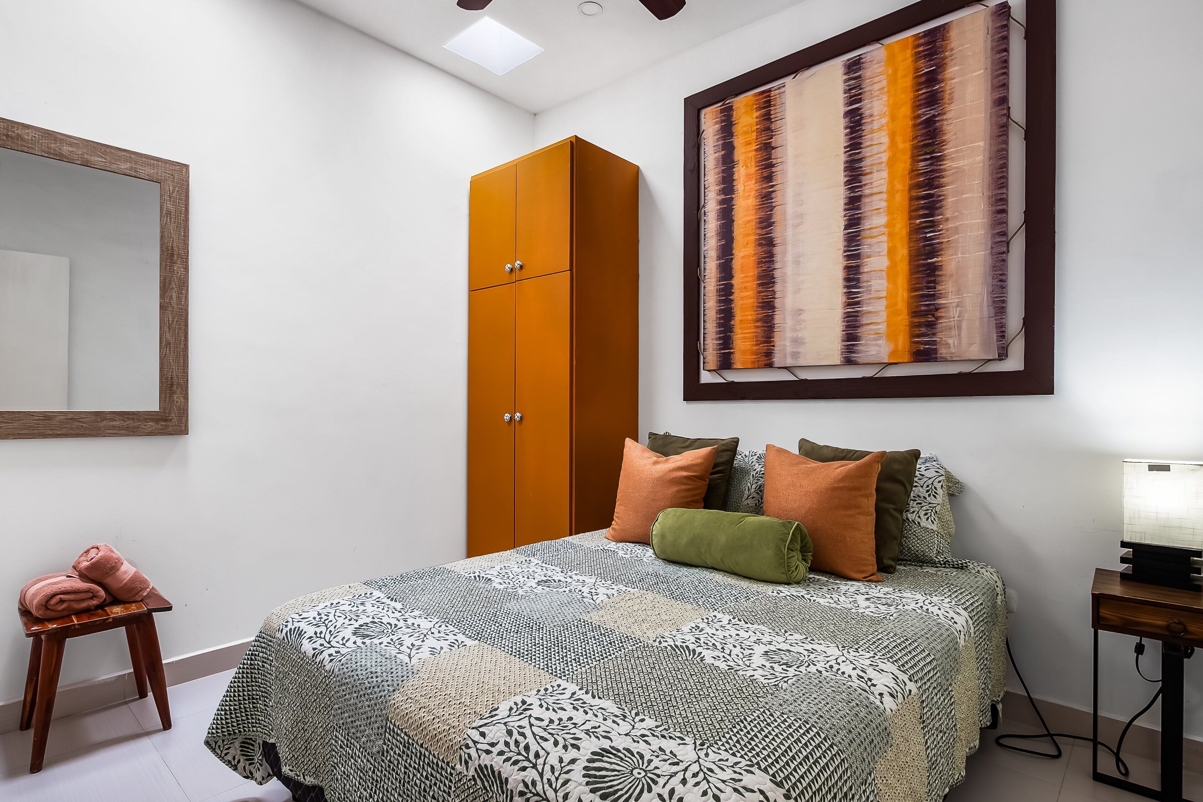 A bedroom with a bed, a wardrobe, a mirror, and a wall art piece.