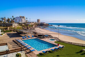 A poolside view with a clear blue sky, a sandy beach, and a rocky coastline. - Dog-friendly Home With Partial Ocean View, Heated Pool, Rooftop Terrace (Playas de Rosarito)