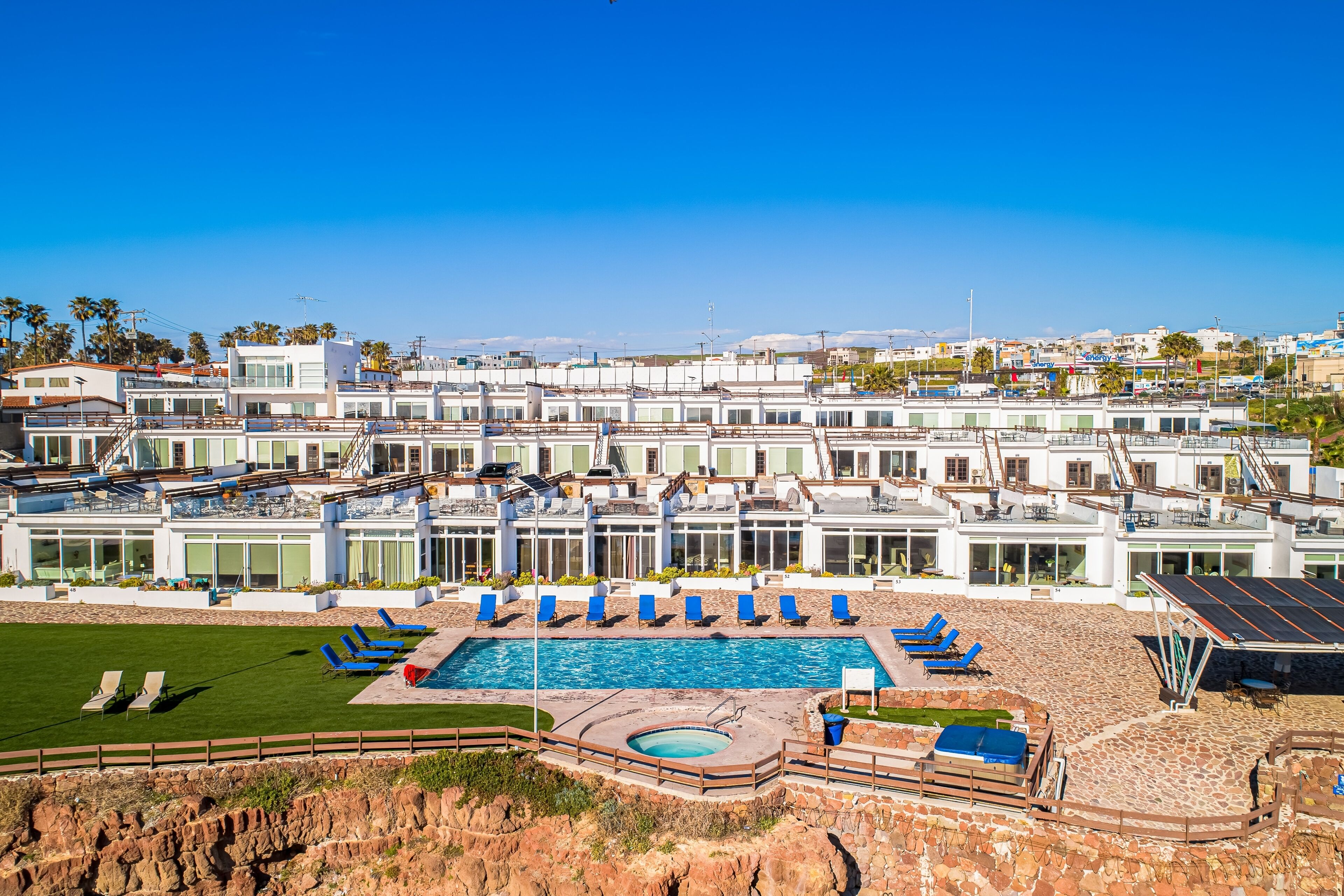 Um hotel moderno com uma ampla área de piscina, diversas espreguiçadeiras e vista para a paisagem ao redor.