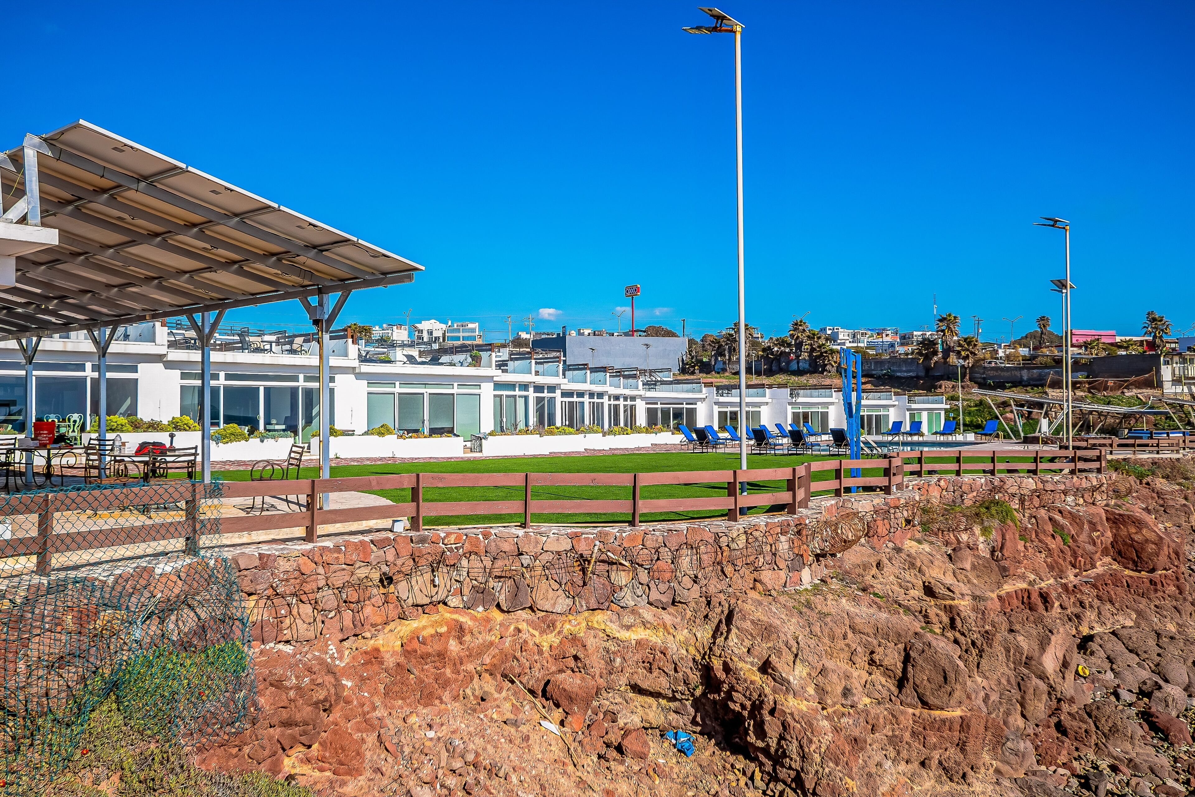 A coastal hotel with a covered outdoor seating area, a stone retaining wall, and a view of the beach and ocean.