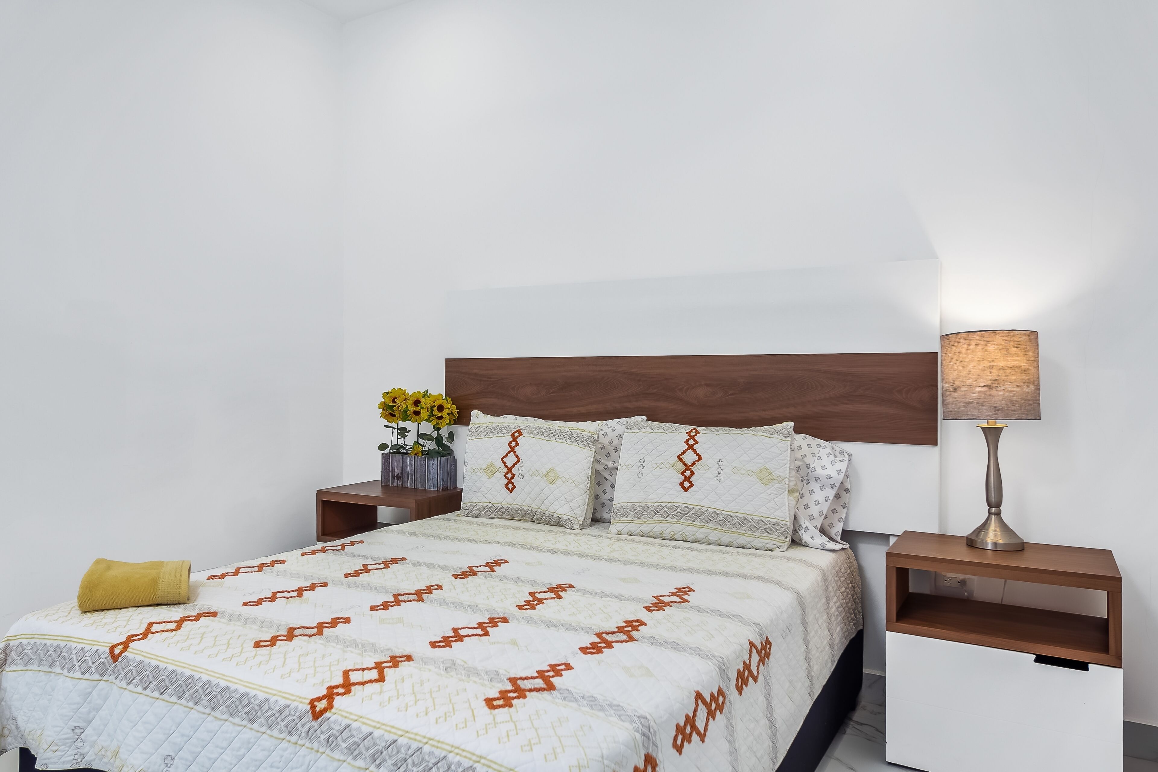A neatly made bed with a patterned bedspread, a wooden headboard, and a bedside lamp.
