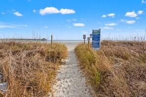 Ein Strandweg führt zum Meer, mit Schildern, die auf einen Fußweg und Zugang zum Strand hinweisen.