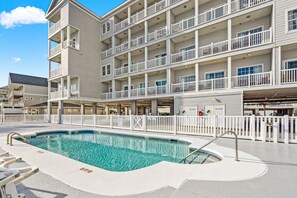 Ein mehrstöckiges Hotel mit Schwimmbad, Balkonen und einem eingezäunten Poolbereich.