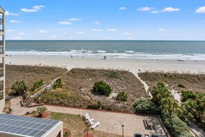 Blick auf einen Strand von einem Gebäude aus, mit einem Weg zu einer Sitzgelegenheit.