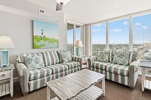 A living room with striped sofas, a coffee table, and a painting of a lighthouse. - Bahama Sands 901- a luxury ocean view condo in North Myrtle Beach (North Myrtle Beach)