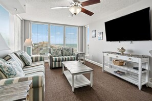 A living room with a sofa, armchair, coffee table, TV, and a ceiling fan. - Bahama Sands 901- a luxury ocean view condo in North Myrtle Beach (North Myrtle Beach)