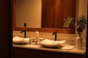 A bathroom with two vessel sinks, a towel, a soap dispenser, and a potted plant.