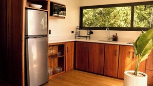 A kitchen with wooden cabinets, a stainless steel refrigerator, a window with a view of trees, and a potted plant. - Villa Tucán - Nuakú Jungle (San Carlos)