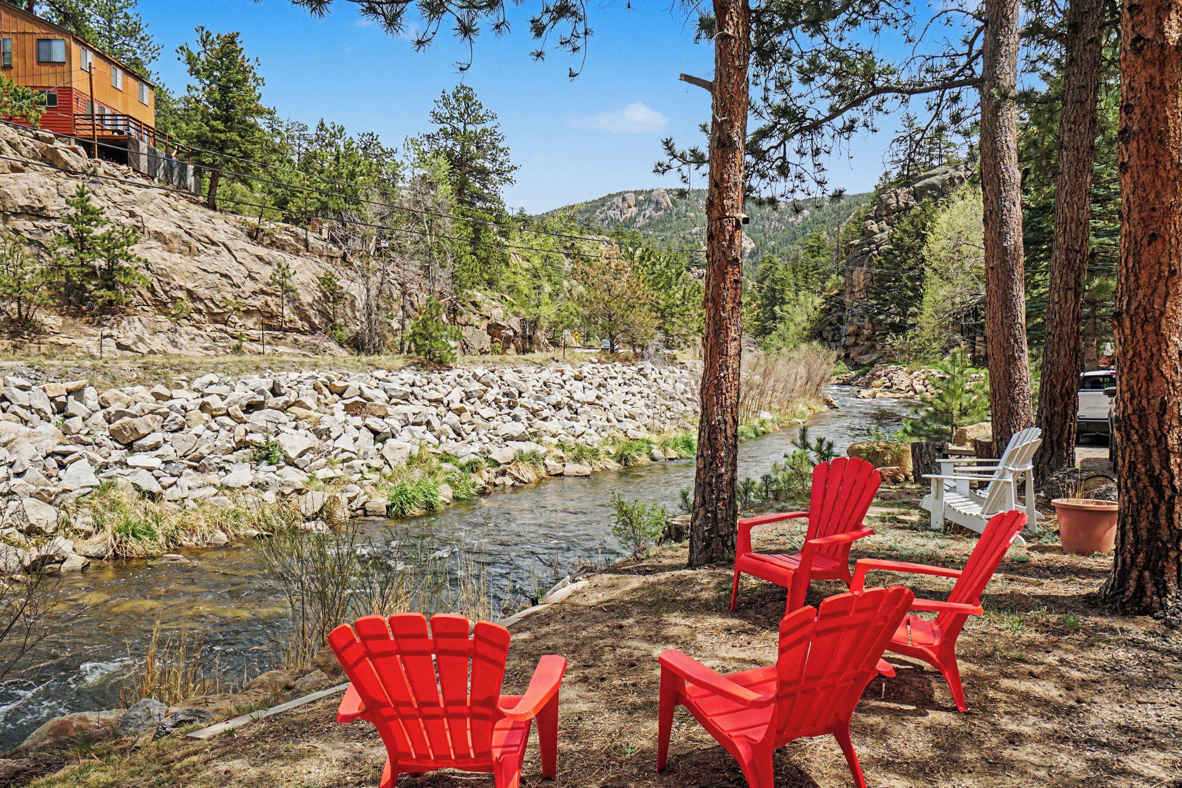 A peaceful riverside retreat with towering pines and mountain views framing your private seating area, perfect for unwinding to the sound of flowing water.