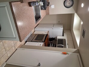 Eine kleine Küche mit Spüle, Herd, Kühlschrank und einer Wanduhr.