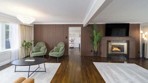 Un salon moderne avec une cheminée, deux fauteuils verts, une table basse et un téléviseur fixé au mur.