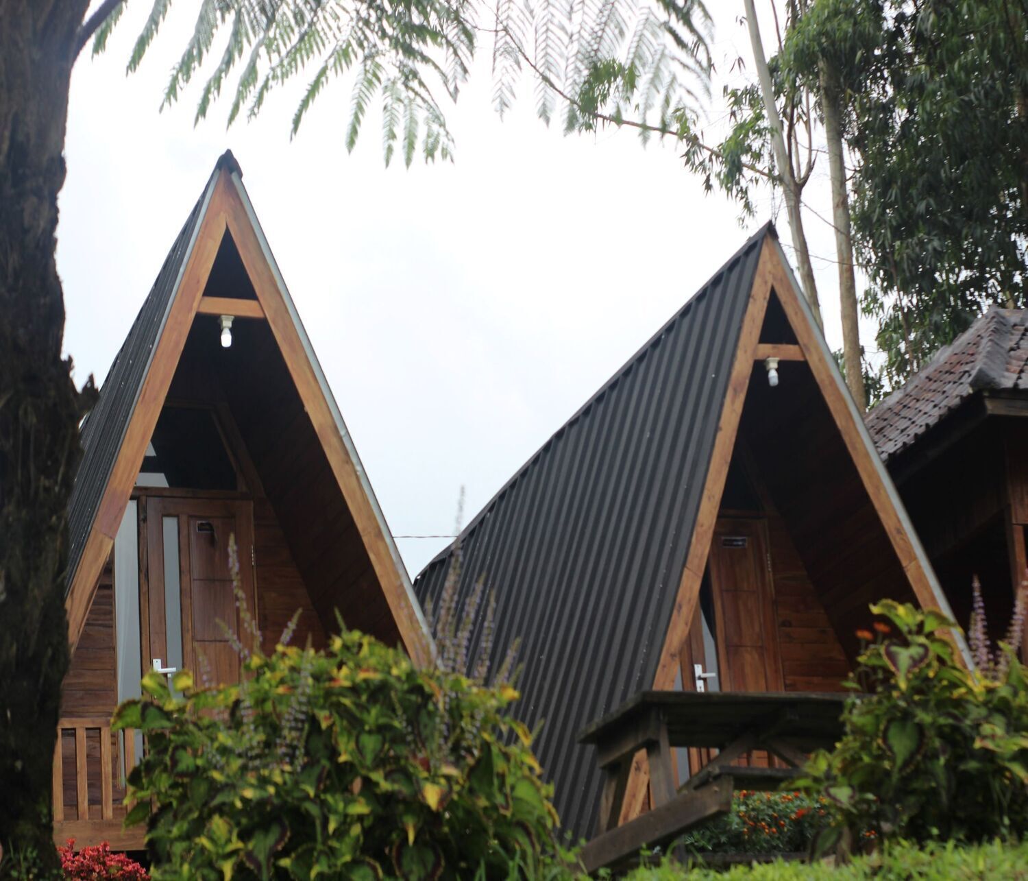 Two triangular wooden cabins with metal roofs, surrounded by greenery.