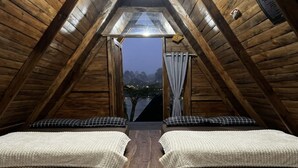 A cozy attic bedroom with wooden walls, a sloped ceiling, two beds with checkered bedding, and a view of a body of water. - Cozzy Villa Hajeka (Pangalengan)
