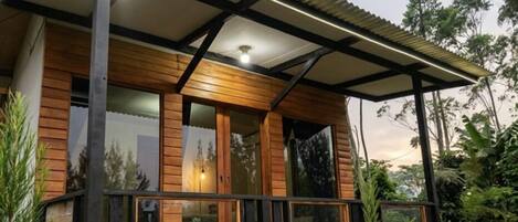 A wooden cabin with a balcony, large windows, and a covered porch area.