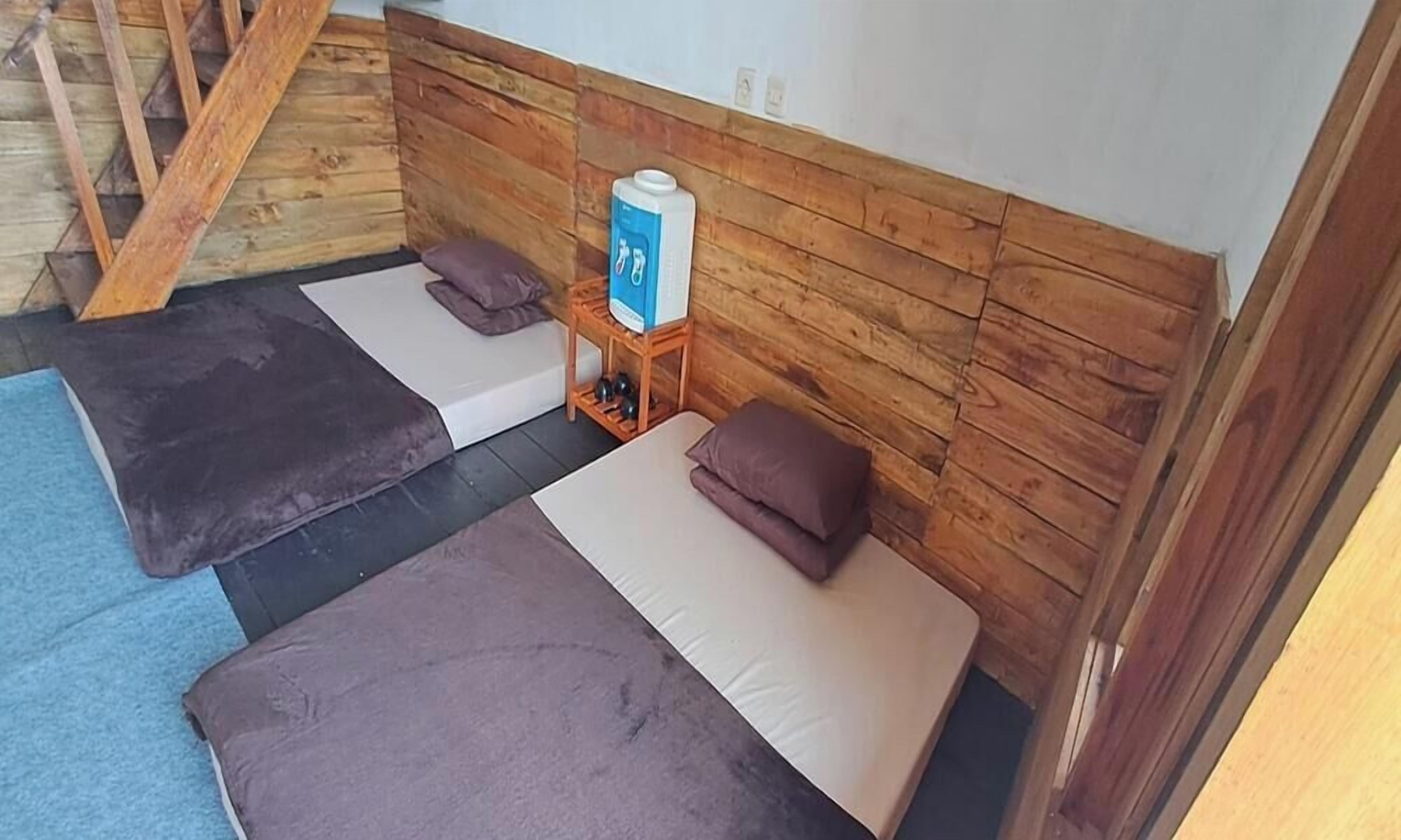 Una habitación con dos camas, un cabecero de madera, una mesita con dispensador de agua y una escalera.