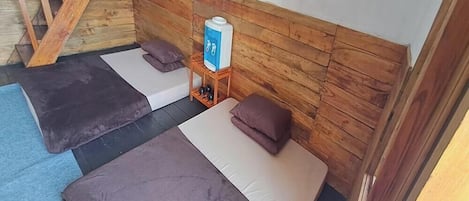 Una habitación con dos camas, un cabecero de madera, una mesita con dispensador de agua y una escalera.