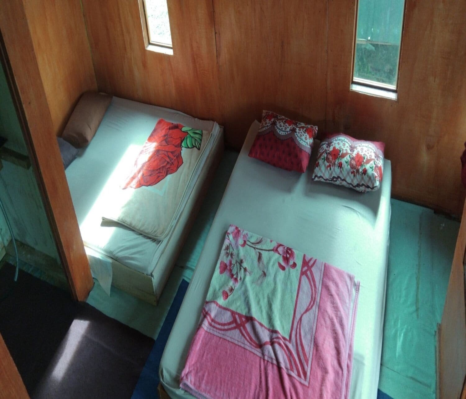 Two single beds with floral bedding and pillows, wooden walls, and a window.