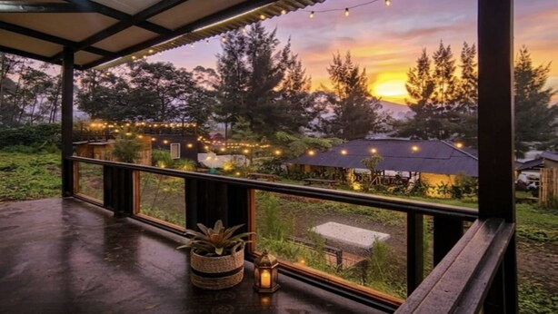 A covered outdoor area with a view of a sunset, string lights, and a wooden deck. - Cozzy Villa Hajeka (Pangalengan)