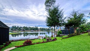 A well-maintained grassy area with a pond, trees, and a small building. - Cozzy Villa Hajeka (Pangalengan)