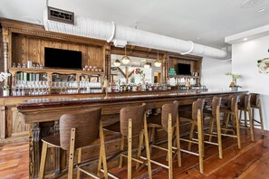 A bar area with wooden bar stools, a long counter, and a television screen. - Commander 6 Farragut Lofts, Old Town, City Park (Bay Saint Louis)