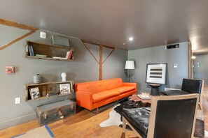 A room with a wooden floor, a sofa, a desk, a lamp, a framed picture, and a shelf with books and decorative items. - Commander 6 Farragut Lofts, Old Town, City Park (Bay Saint Louis)