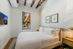 Ein Schlafzimmer mit einem großen Bett, einem Fenster mit Blick, gerahmten Kunstwerken und einem Nachttisch mit Lampe.