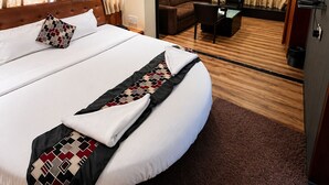 A hotel room with a large bed, a ceiling fan, a desk with a chair, and a television. - Glitz Hotel Jayshree - Nr Mumbai Airport (Mumbai)