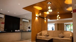 A reception area with a wooden reception desk, a sofa, and a coffee table. - Glitz Hotel Jayshree - Nr Mumbai Airport (Mumbai)