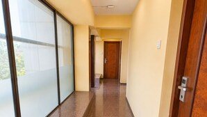 A corridor with a glass wall on one side, a wooden door on the other, and a tiled floor. - Glitz Hotel Jayshree - Nr Mumbai Airport (Mumbai)