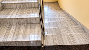 A staircase with marble steps and a metal handrail, leading to a landing with a yellow wall and a patterned light fixture. - Glitz Hotel Jayshree - Nr Mumbai Airport (Mumbai)