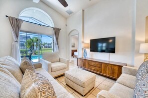Ein Wohnzimmer mit Sofa, Hocker und einem an der Wand befestigten Flachbildfernseher.