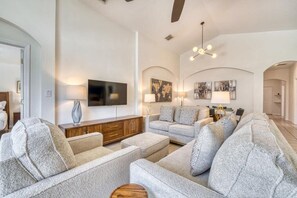 Ein modernes Wohnzimmer mit Flachbildfernseher, grauen Sofas, einem Holzschrank und einer Kristallleuchter.