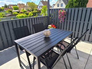 Ein dunkles Holztisch mit einer dekorativen Vase und Stühlen auf einer Terrasse.